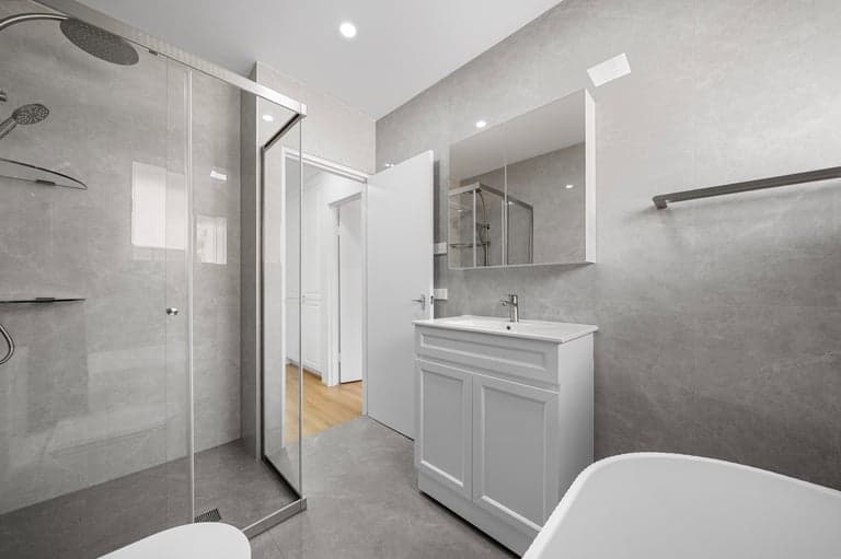 Grey tiled family bathroom in Sydney with a white vanity, shower screen and bath