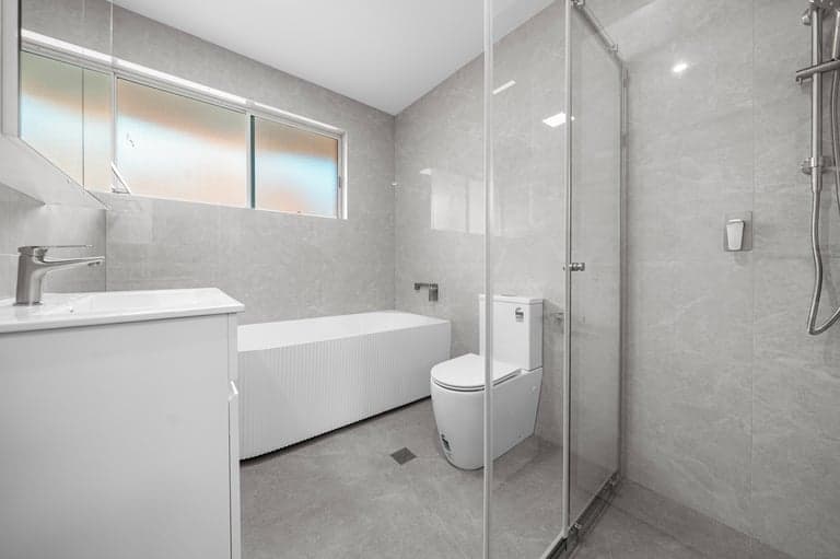 Grey Sydney bathroom with a ribbed bath, white vanity and glass shower