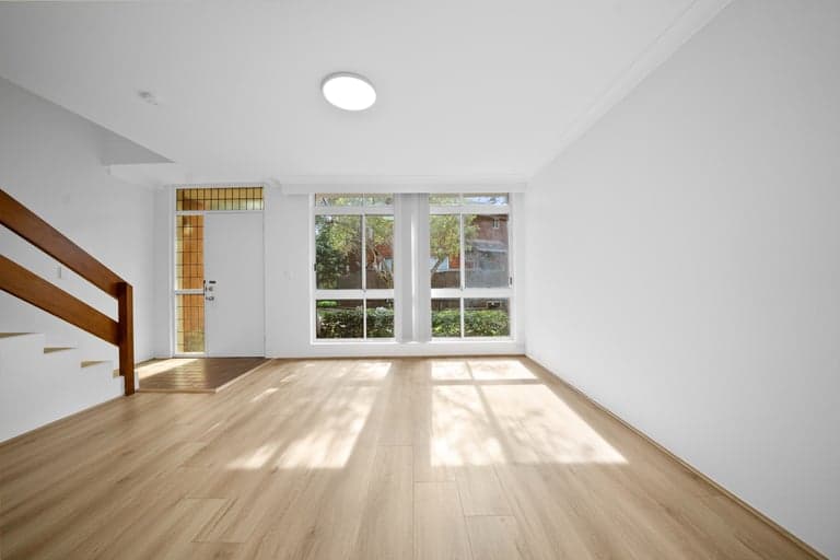 Sunlit oak flooring in a Sydney living room with twin windows and a timber stair rail