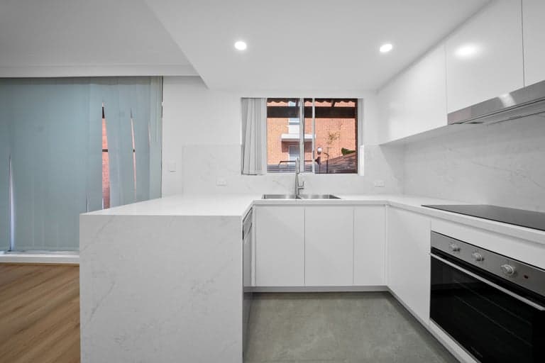 White handleless corner kitchen in Sydney with a stone bench, cooktop and oven