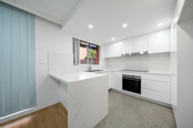 White peninsula kitchen renovation in Sydney with stone benchtops and a wall oven