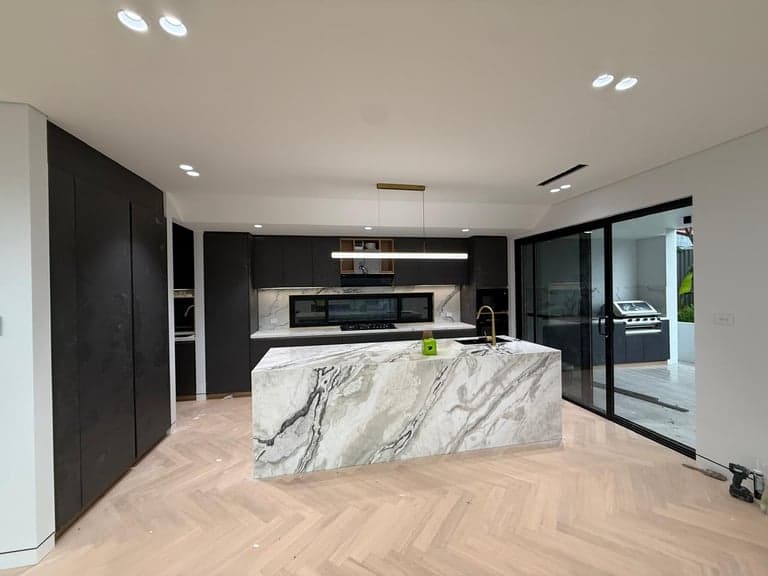 Dark joinery kitchen in Sydney with a marble island, linear pendant and herringbone oak floors