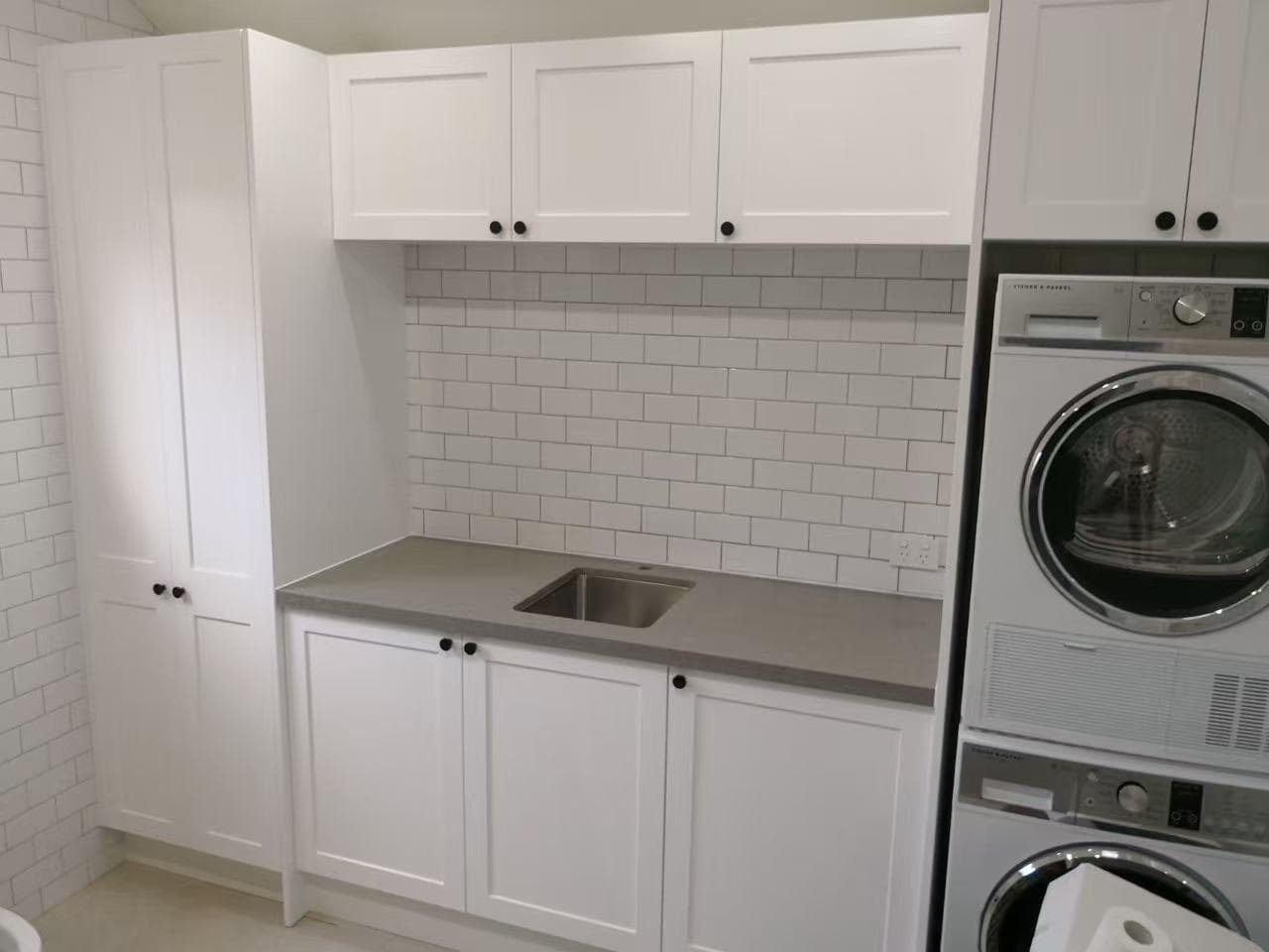 Modern laundry with black cabinets, stone bench and paired machines