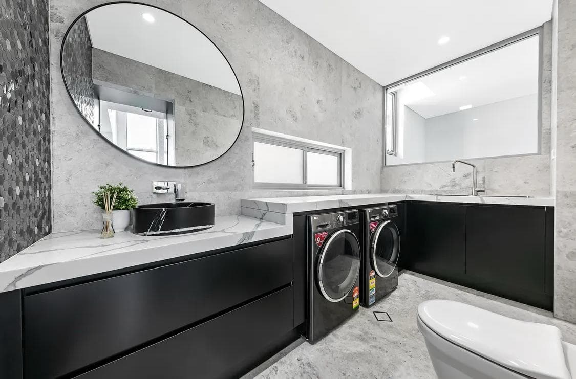 Modern Sydney laundry renovation with black cabinets, a stone bench and paired machines