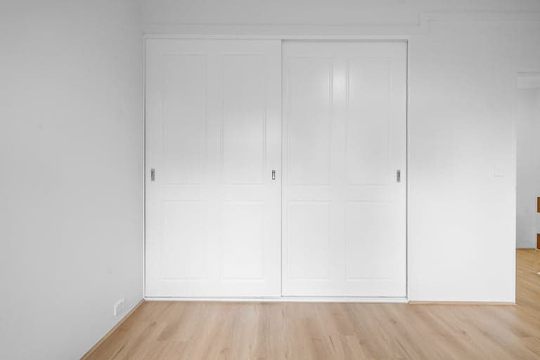 White sliding wardrobe doors in a bright Sydney bedroom with oak floors